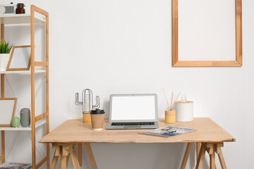 Modern laptop on wooden standing desk near light wall