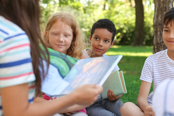 Fototapeta na wymiar Teacher reading book to her little pupils in park