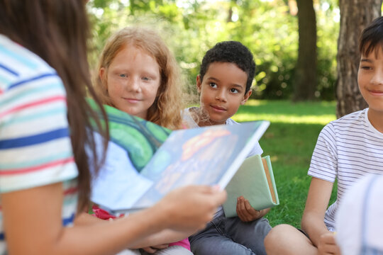 Teacher reading book to her little pupils in park
