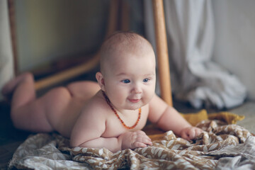 cute european baby 5 months old lies on a blanket on the floor. A child wearing amber teething beads in a real interior