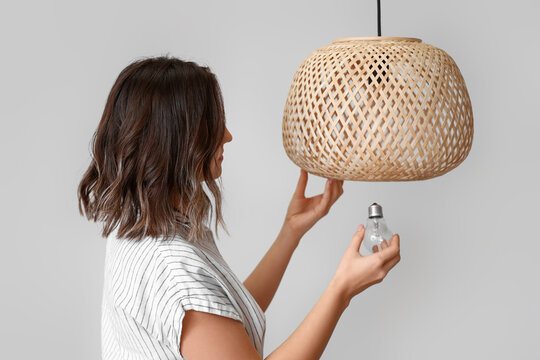 Woman changing light bulb in hanging lamp near light wall