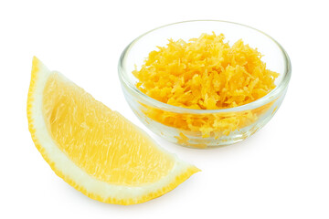 Grated lemon zest in a glass bowl next to lemon segment.