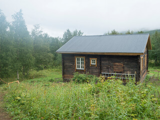 View of STF Njunjes Mountain cabin on a meadow, moody rainy day with thick fog. Wooden cottage lies on the banks of the Tarra river, at Padjelantaleden hiking trail. Lapland summer landscape