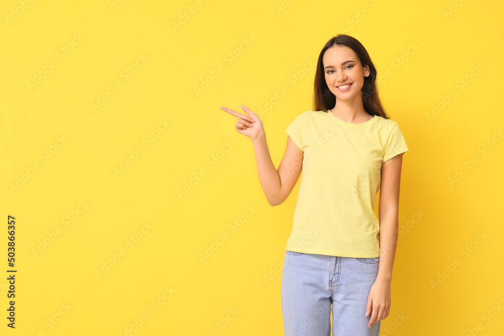Wall mural Pretty young woman in stylish t-shirt pointing at something on yellow background - Wall murals