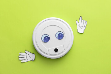 Modern robot vacuum cleaner with drawn eyes and paper hands on green background