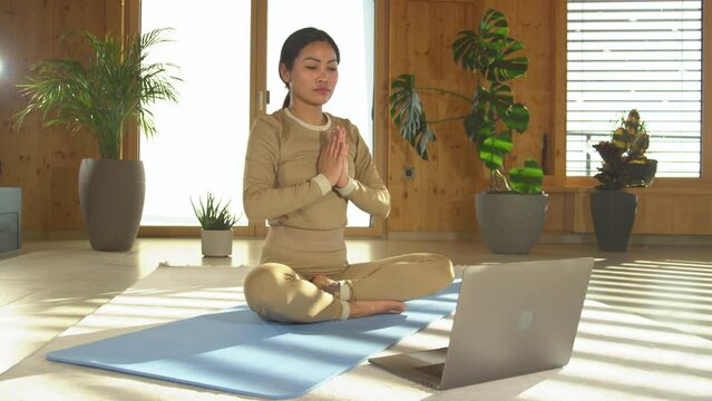 STILL SHOT: Asian female yoga instructor beginning an online yoga training class. Beautiful Philippine woman explaining and changing poses while teaching yoga in an online live video exercise course.