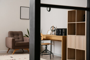 Modern speakers, headphones and blank photo frame on wooden table in room interior, view through partition