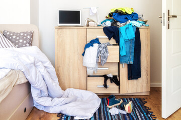 mess in a teenager's room. Clothes are strewn across the chest of drawers, floor
