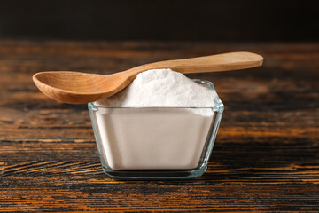 Bowl of baking soda and spoon on wooden background