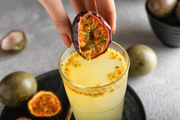 Woman squeezing passion fruit in glass on grey background - obrazy, fototapety, plakaty