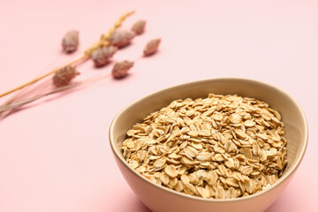 Bowl of raw oatmeal on pink background, closeup