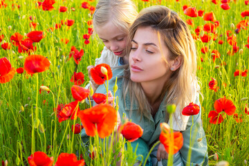 Obraz na płótnie Canvas Woman with child girl in field with red poppies. Mother and daughter are playing in the field of flowering red poppies.