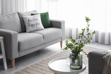 Vase with beautiful blooming tree branches and glass with water on table in living room