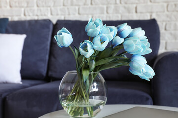 Glass vase with blue tulips on table in living room, closeup