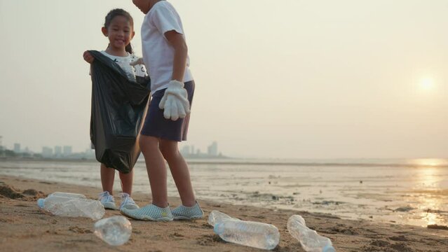 Volunteer happy family kids picking plastic bottle into trash plastic bag black for cleaning beach, children clean up garbage at sunset, Ecology and World Environment Day, Save earth concept