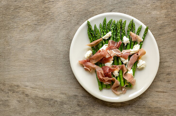 Plate with green asparagus with mozzarella cheese and prosciutto ham