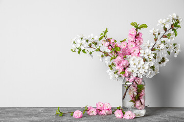 Glass vase with beautiful blooming branches on table near light wall