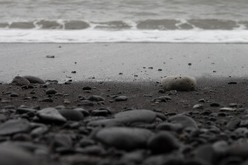 Fototapeta na wymiar Black volcanic beach with surf wave, black sand, cobbles as lines with blur, texture, background.