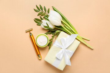 Facial massage tool with jar of cream, gift box and tulips on beige background. Mother's Day celebration