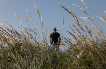 Rear view of adult man standing between grasses against sky
