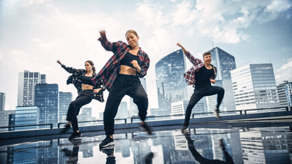 Diverse Group of Three Professional Dancers Performing a Hip Hop Dance Routine in Front of a Big Digital Led Wall Screen with Modern Urban Skyline with Skyscrapers in Studio Environment.