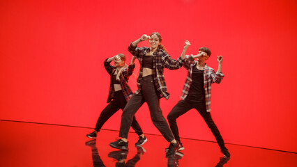 Diverse Group of Three Professional Dancers Performing a Hip Hop Dance Routine in Front of a Big Digital Led Wall Screen with Deep Orange and Red Color Background in Studio Environment.