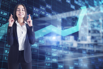 businesswoman with crossed fingers standing in office interior with creative digital financial numbers or index data on blurry background with growin arrow. Stock market and growth concept. 