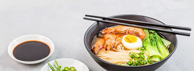 Asian noodle soup, ramen with prawn shrimp, vegetables and egg in black bowl on gray concrete background. Flat lay, Top view, mock up, overhead. Healthy food concept
