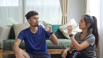 Healthy young couple in sportswear resting and drinking water after morning workout.