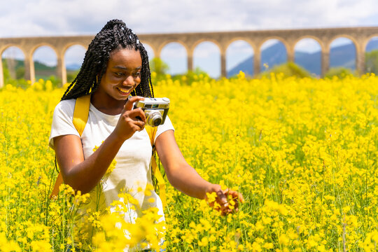Taking photos with a vintage camera, a black ethnic girl with braids, a traveler, in a field of yellow flowers