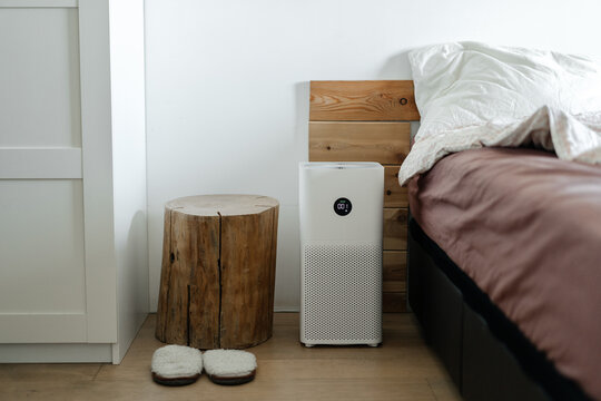 air purifier with a stylish modern design sits on the bedroom floor next to the bed. Air purification, health and technology.