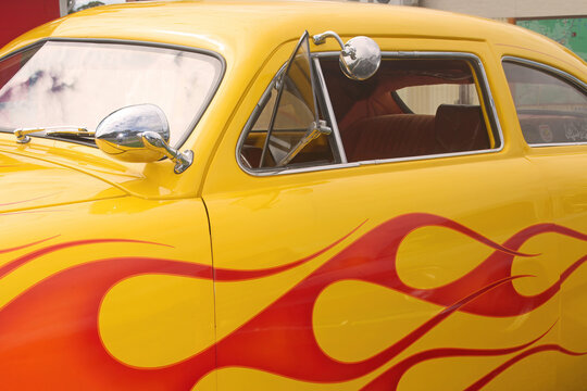 Side of classic vintage car with flames painted on the side. The hot rod has chrome side mirrors and window.