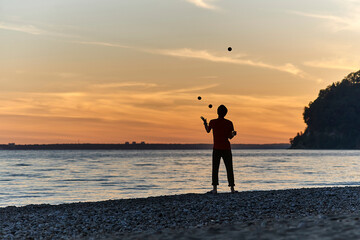 Fototapeta premium The guy stands on the seashore at sunset and juggles with fruits