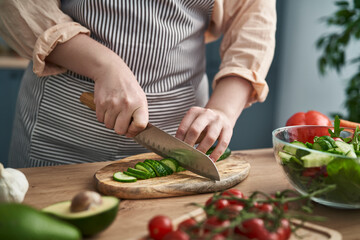 Close up of hands of woman cutting cucumber at the kitchen - Powered by Adobe