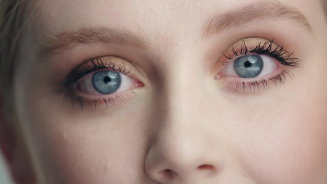 Extreme close up pan beautiful model's bright blue eyes open and look to camera