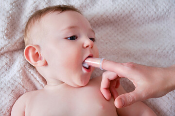 Mother hands brushing teeth with a finger brush of a happy infant baby. Mom doing oral hygiene to a...