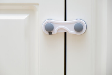 Doors of white kitchen cabinets blocked from children. Lock furniture drawers from toddler baby