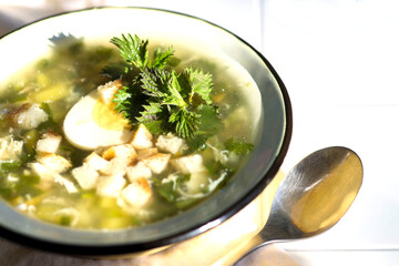 Soup with fresh nettles, egg, meat and potatoes. Fresh nettle leaf on the kitchen table a rustic background.