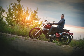 Motorcyclist is sitting on the motorbike outdoors at sunset.