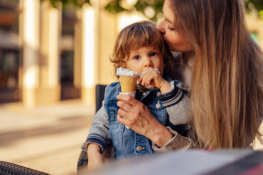 Male Toddler Getting Kisses On The Head From His Mom While Eating Ice Cream.