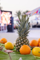 tropical fruit banana orange pineapple in front with beach and colourful umbrellas at back out of focus with grain