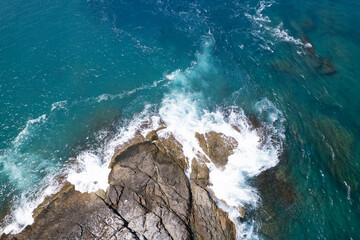 Aerial view Drone camera top down of seashore rocks in a blue ocean Turquoise sea surface Amazing sea waves crashing on rocks seascape. High quality image of sea waves in Phuket Thailand