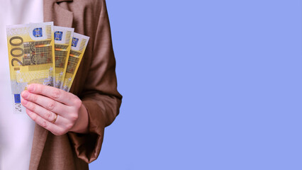 Woman teacher holding money in bills of 200 euros in her hands on a blue background, banner close-up