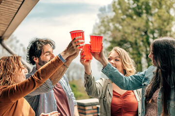 friends drinking and toasting on plastic cups - young people having fun together outdoors - obrazy, fototapety, plakaty