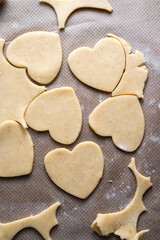 The process of cooking heart cookies. Top view of raw dough, rolling pin and baking cutters. Dark background