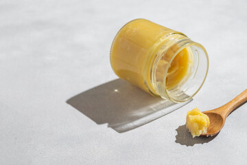 Ghee in a glass jar made with sunflower oil on a light background, copy space for text. Hard light.