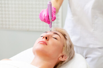 Obraz na płótnie Canvas A beutician in medical pink gloves does mesotherapy to a woman's forehead. Hardware professional cosmetology in a beauty salon