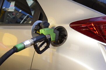 Refueling modern car with petrol pump on gas station, closeup. White car refueling at gas station with green fuel nozzle. refueling gun in the tank 