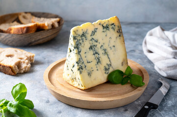 Blue cheese, dor blue or roquefort mold cheese slice on cutting board with basil leaves, lifestyle...