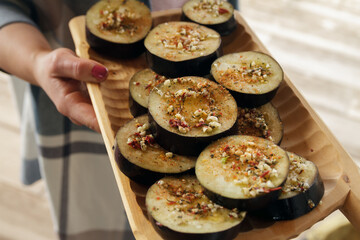 Woman hand holding a wooden plate or platter of eggplant with garlic and spices. Delicious vegetables ready for barbecue grill cooking.